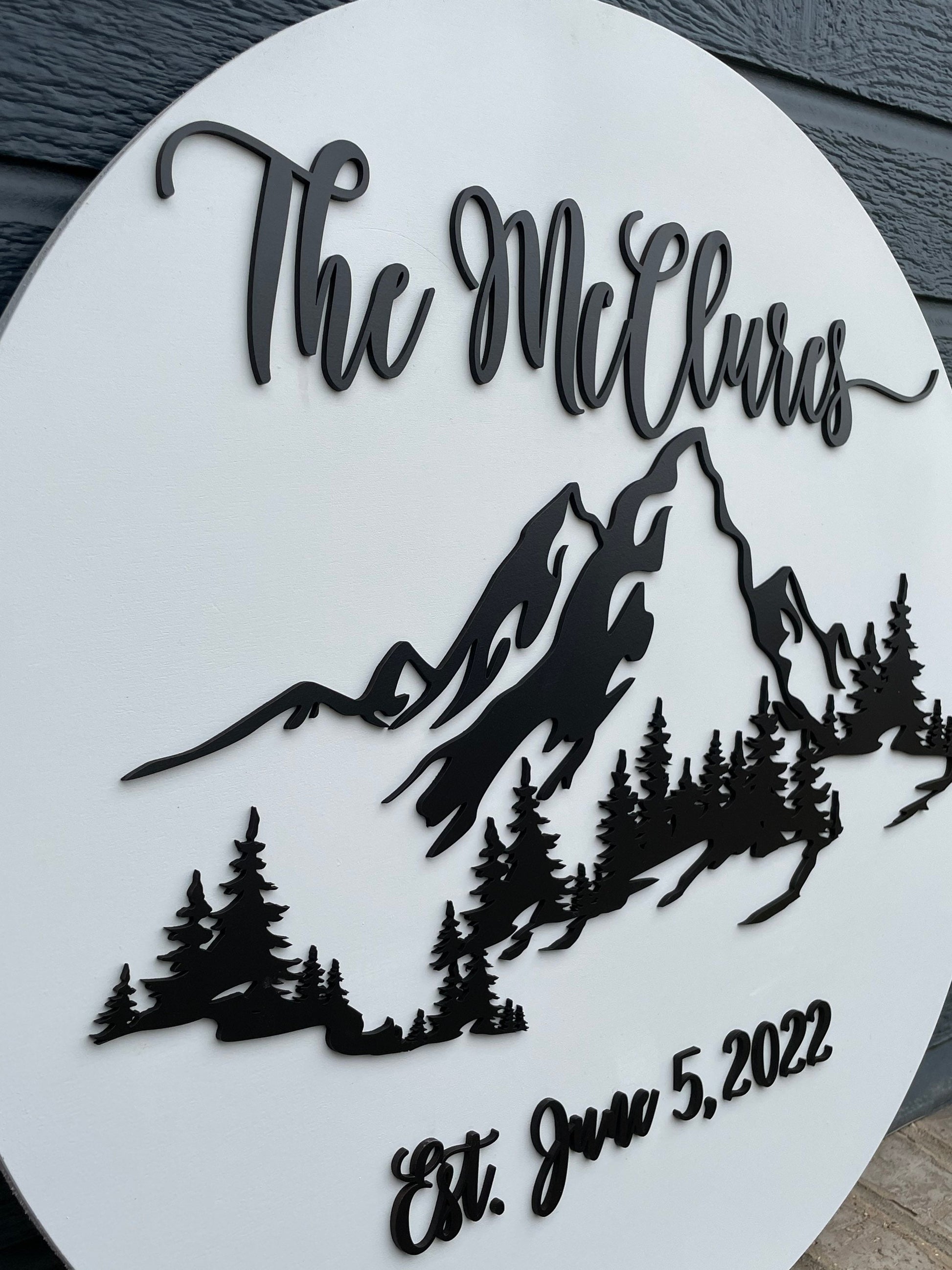 Up close view of 3D Black and white wooden wedding guestbook with trees and a mountain range. Include family name and wedding date.